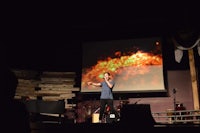 a man standing on stage in front of a projection screen